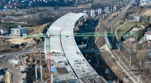 Budowa nowej estakady drogowej w mieście, z widocznymi dźwigami i torami kolejowymi w tle.