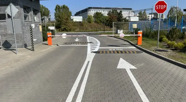 Wyraźne **znaki poziome** kierują ruch na wjeździe, gdzie szlabany i znak STOP zapowiadają kontrolę.