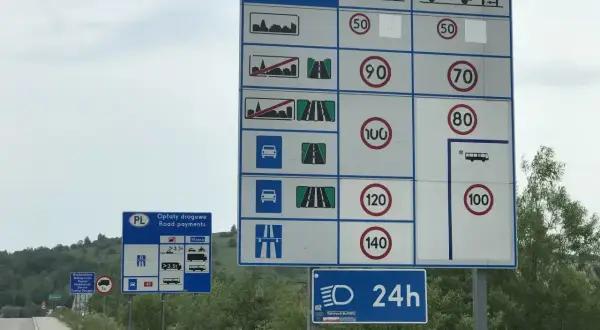 Duży znak drogowy z informacjami o opłatach i ograniczeniach prędkości. Obok mniejszy znak "Opłaty drogowe".