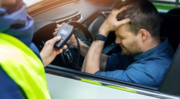 Policjant mierzy kierowcy ile promili. Mężczyzna zmartwiony trzyma się za głowę.