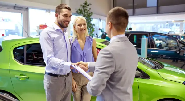 Szczęśliwa para odbiera nowe auto na e. Sprzedawca podaje im dokumenty do podpisania.