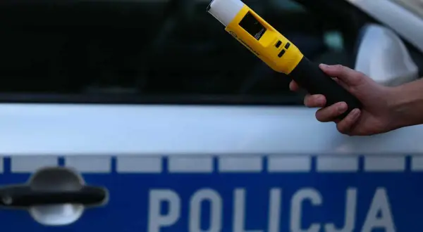 Dłoń trzyma żółty alkomat na tle radiowozu z napisem "POLICJA".