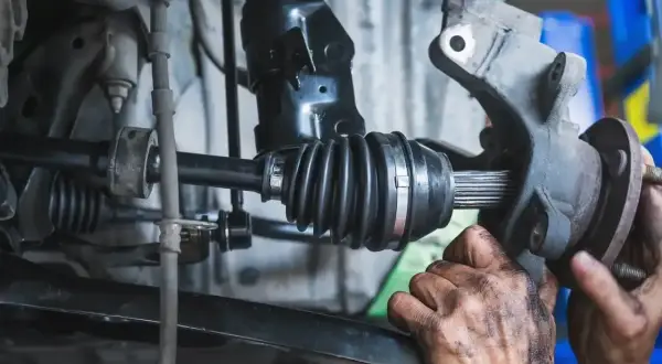 Mechanik wymienia przegub w samochodzie. Widoczny jest wałek napędowy z gumową osłoną i wielowypustem.