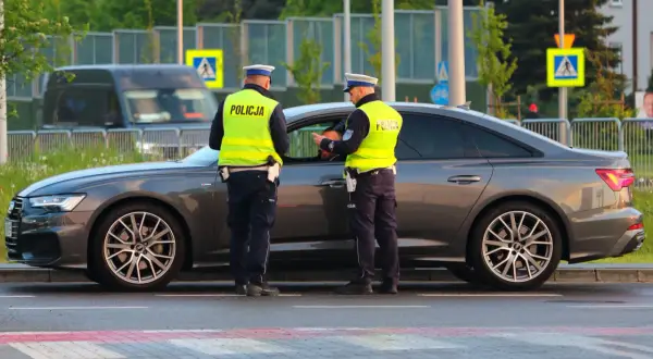 Policjanci w kamizelkach odblaskowych rozmawiają z kierowcą przy samochodzie. Może to być kontrola drogowa lub przygotowanie do odwołania od mandatu.