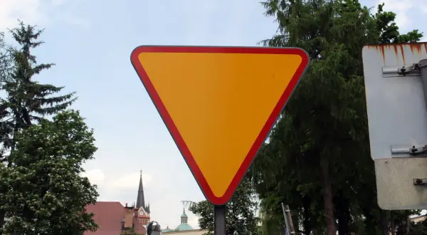 Żółty trójkątny znak a7 z czerwoną obwódką, ostrzegający o ustąpieniu pierwszeństwa.