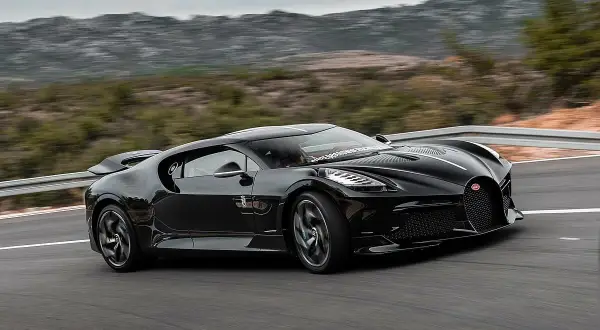 Czarny Bugatti La Voiture Noire, najdroższy samochód świata, pędzi po krętej drodze wśród wzgórz.