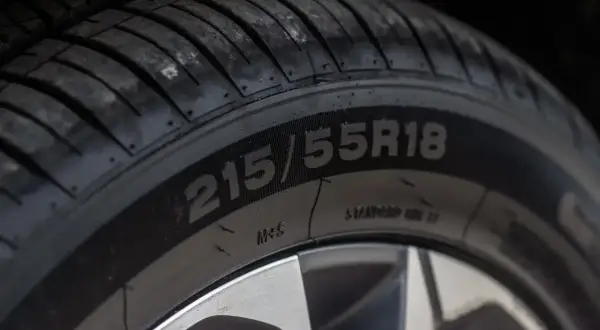 Zbliżenie na oponę z widocznym rozmiarem 215/55R18. Na boku opony można dostrzec oznaczenia dotyczące daty produkcji.