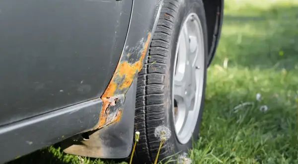 Rdza na progu samochodu, obok opony i kół, na tle zielonej trawy.