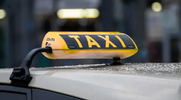 Żółty dachowy znak TAXI na samochodzie, z widocznymi kroplami deszczu.