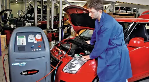 Mechanik sprawdza układ klimatyzacji w czerwonym samochodzie. Urządzenie CoolTech AC550 Pro jest gotowe do pracy, co może wpłynąć na koszt montażu klimatyzacji.