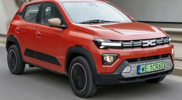 Pomarańczowe Dacia Spring, najtańsze auto elektryczne, jedzie po drodze.