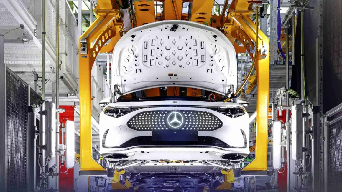Biały samochód elektryczny Daimler na linii produkcyjnej, z otwartą maską i podświetlanym grillem z logo.