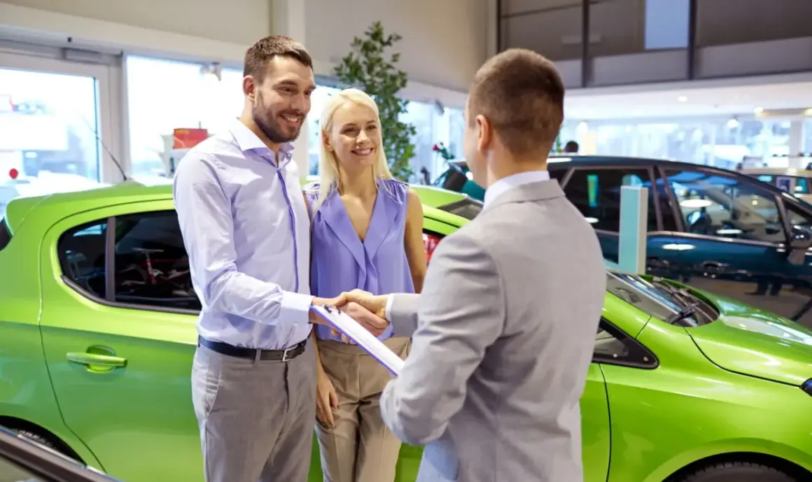 Szczęśliwa para odbiera nowe auto na e. Sprzedawca podaje im dokumenty do podpisania.