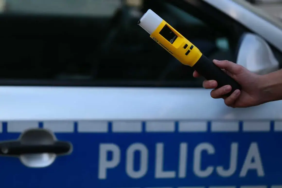 Dłoń trzyma żółty alkomat na tle radiowozu z napisem "POLICJA".