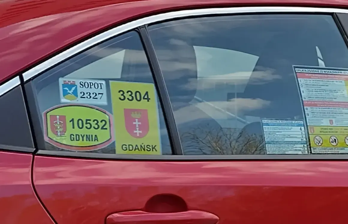 Naklejki taksówkarskie z numerami i herbami miast: Sopot, Gdynia, Gdańsk na czerwonym samochodzie.