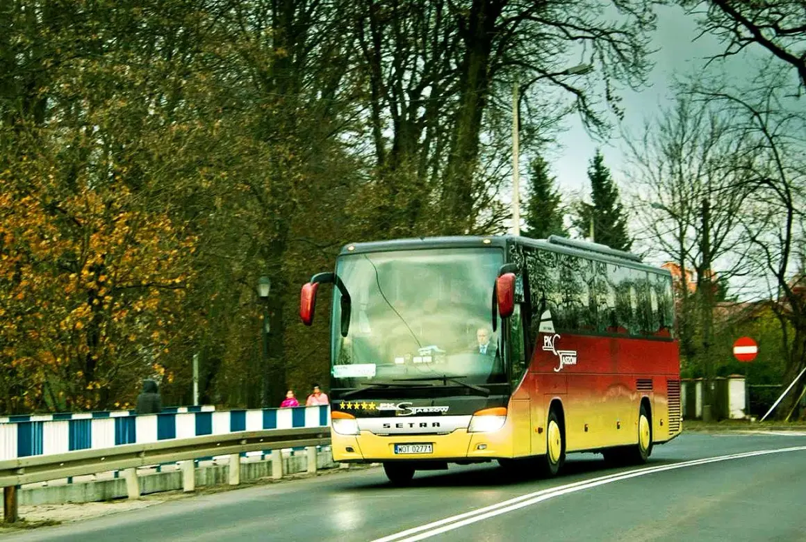 Autobus Bałtyk jedzie drogą wśród drzew.