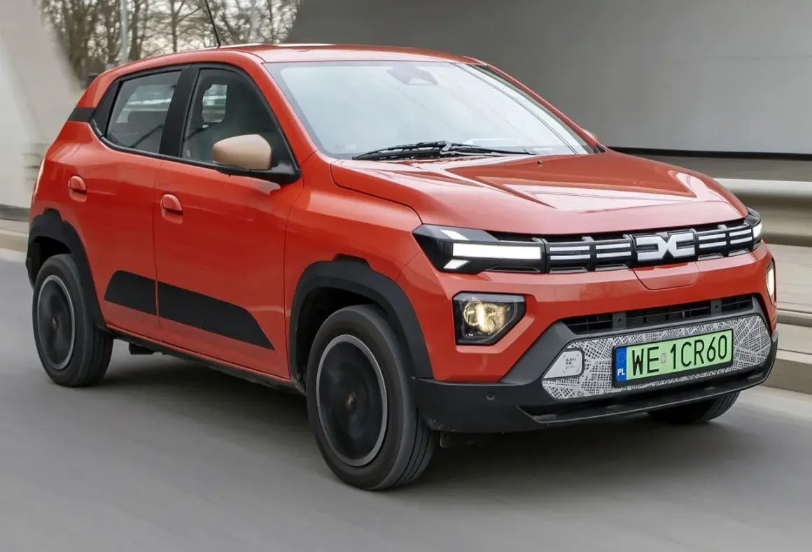 Pomarańczowe Dacia Spring, najtańsze auto elektryczne, jedzie po drodze.