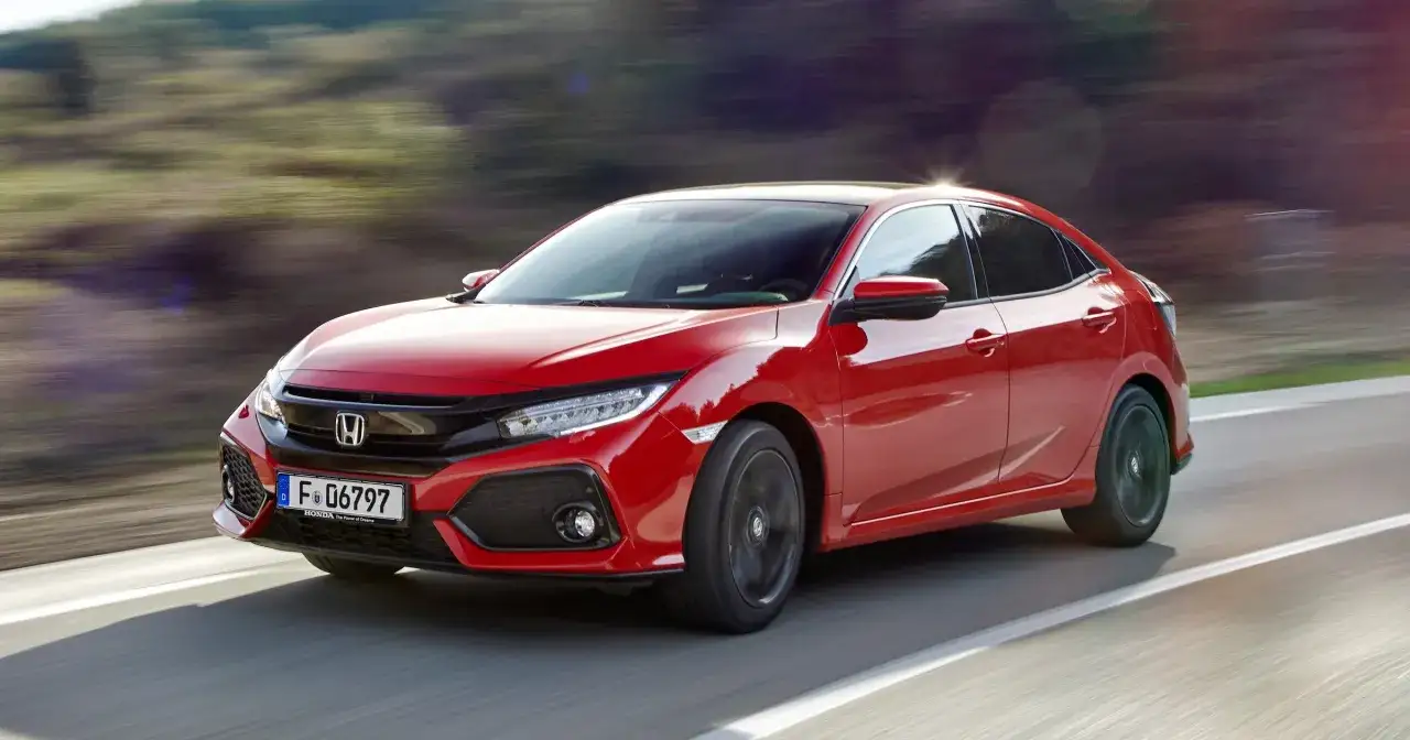 Czerwony Honda Civic Sport pędzi po drodze, otoczony rozmytym tłem zieleni i nieba.