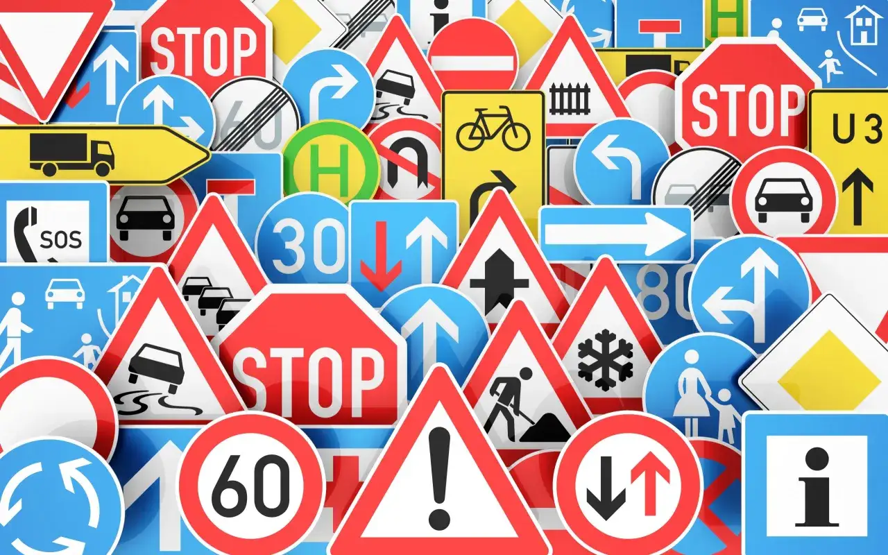 Mnóstwo znaków drogowych: STOP, zakazy, nakazy, ostrzeżenia o robotach drogowych, śliskiej nawierzchni, rowerzystach, pieszych i ograniczeniach prędkości.