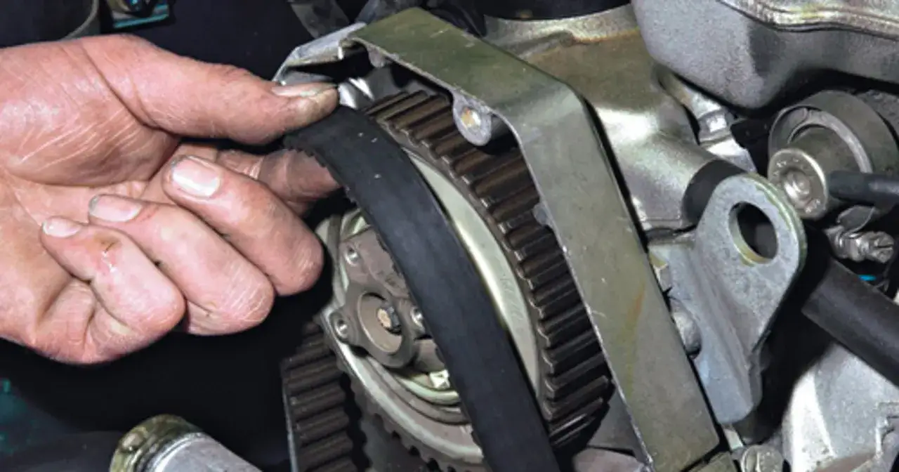 Dłoń mechanika sprawdza stan paska rozrządu podczas jego wymiany.