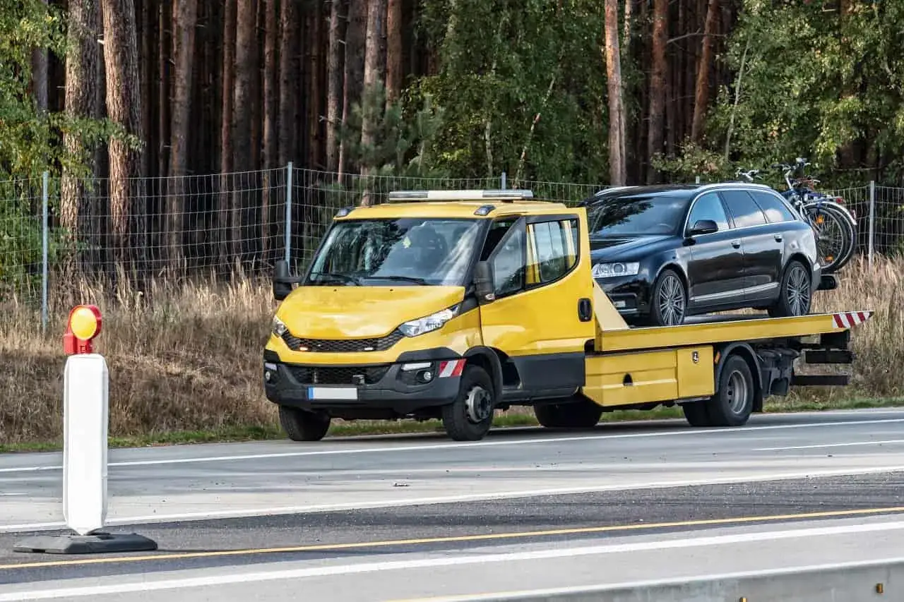Żółta laweta przewozi czarny samochód i rower. To może być konfiskata samochodu lub jego transport.