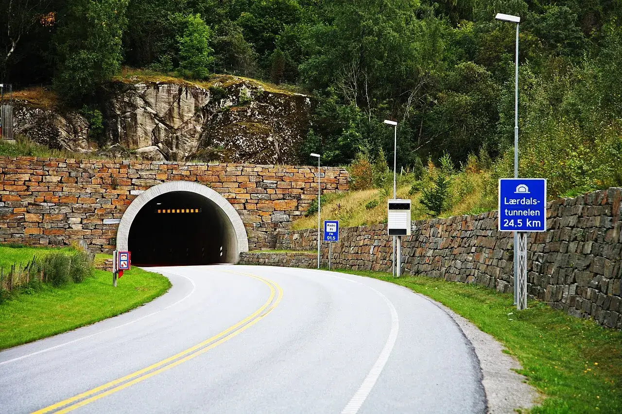Droga prowadzi do Lærdalstunnelen, najdłuższego tunelu na świecie (24,5 km). Kamienna ściana i zielone wzgórza otaczają wejście.
