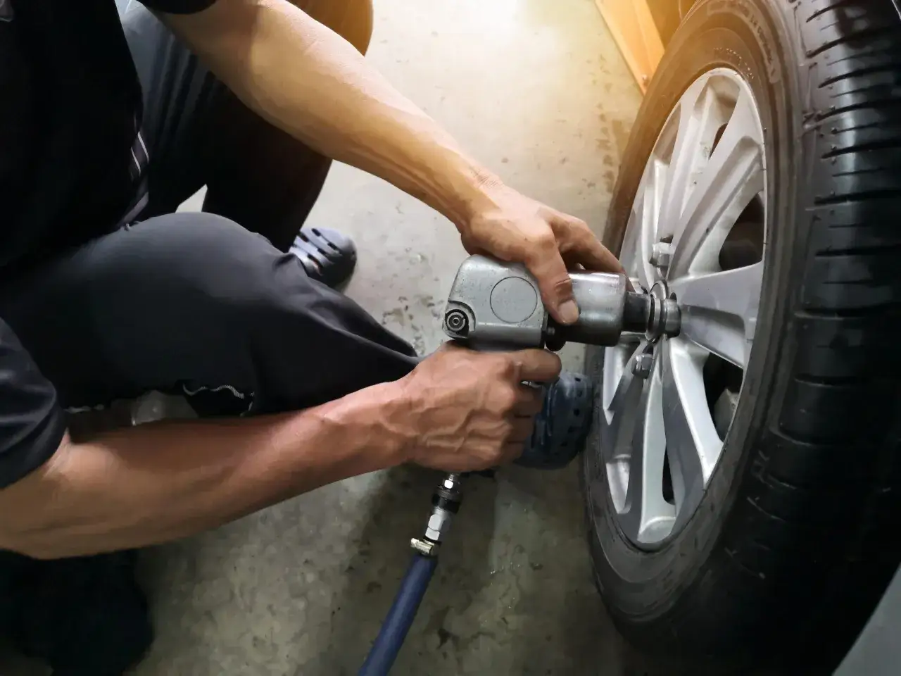 Mechanik dokręca śruby kluczem pneumatycznym podczas wymiany opon. Dowiedz się, ile kosztuje wymiana opon.