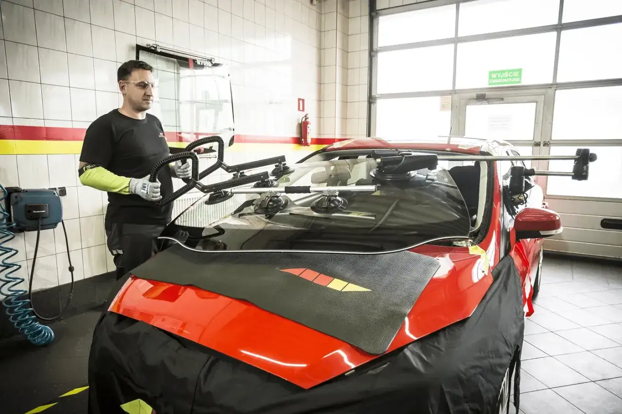 Mechanik w rękawicach i okularach przygotowuje się do klejenia szyb samochodowych, trzymając specjalny uchwyt z przyssawkami.