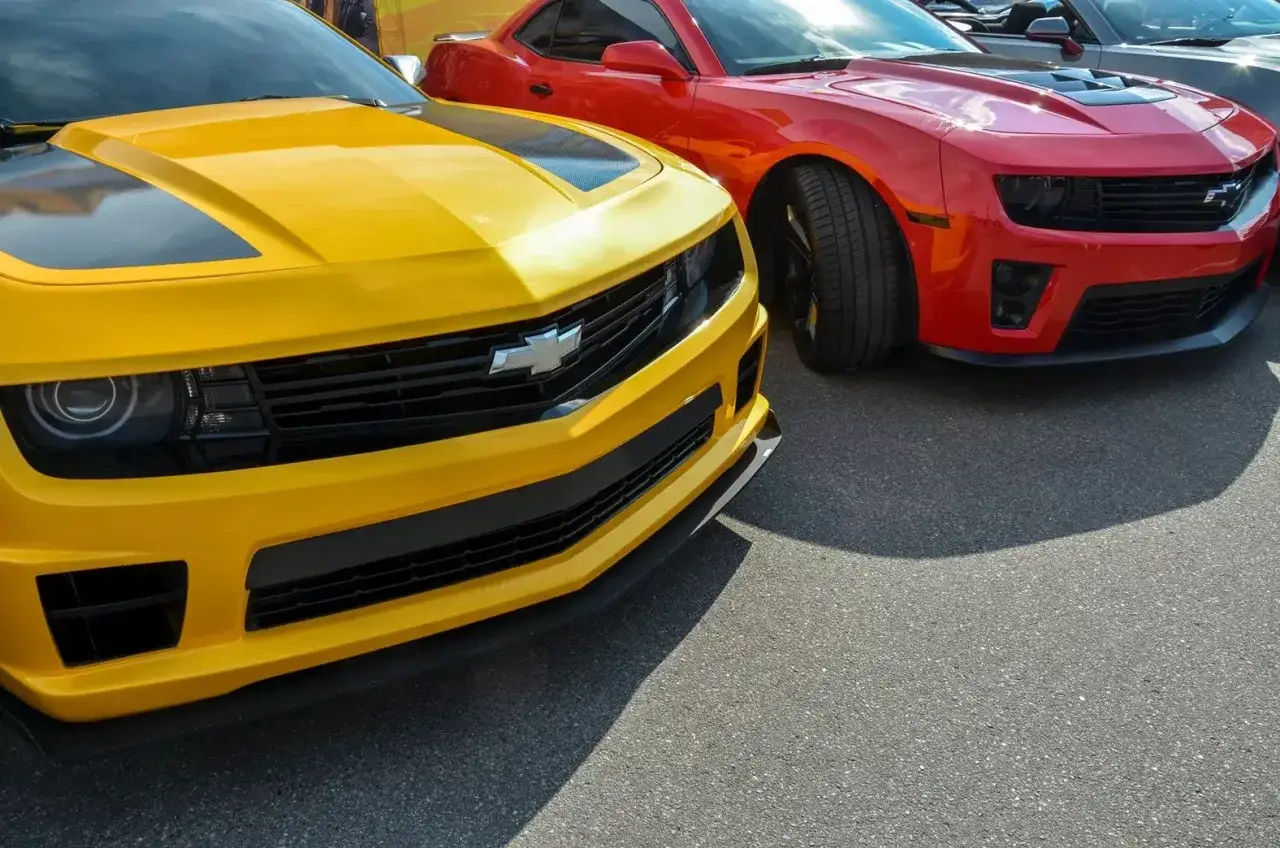 Dwa amerykańskie samochody, żółty i czerwony Chevrolet Camaro, stoją obok siebie.