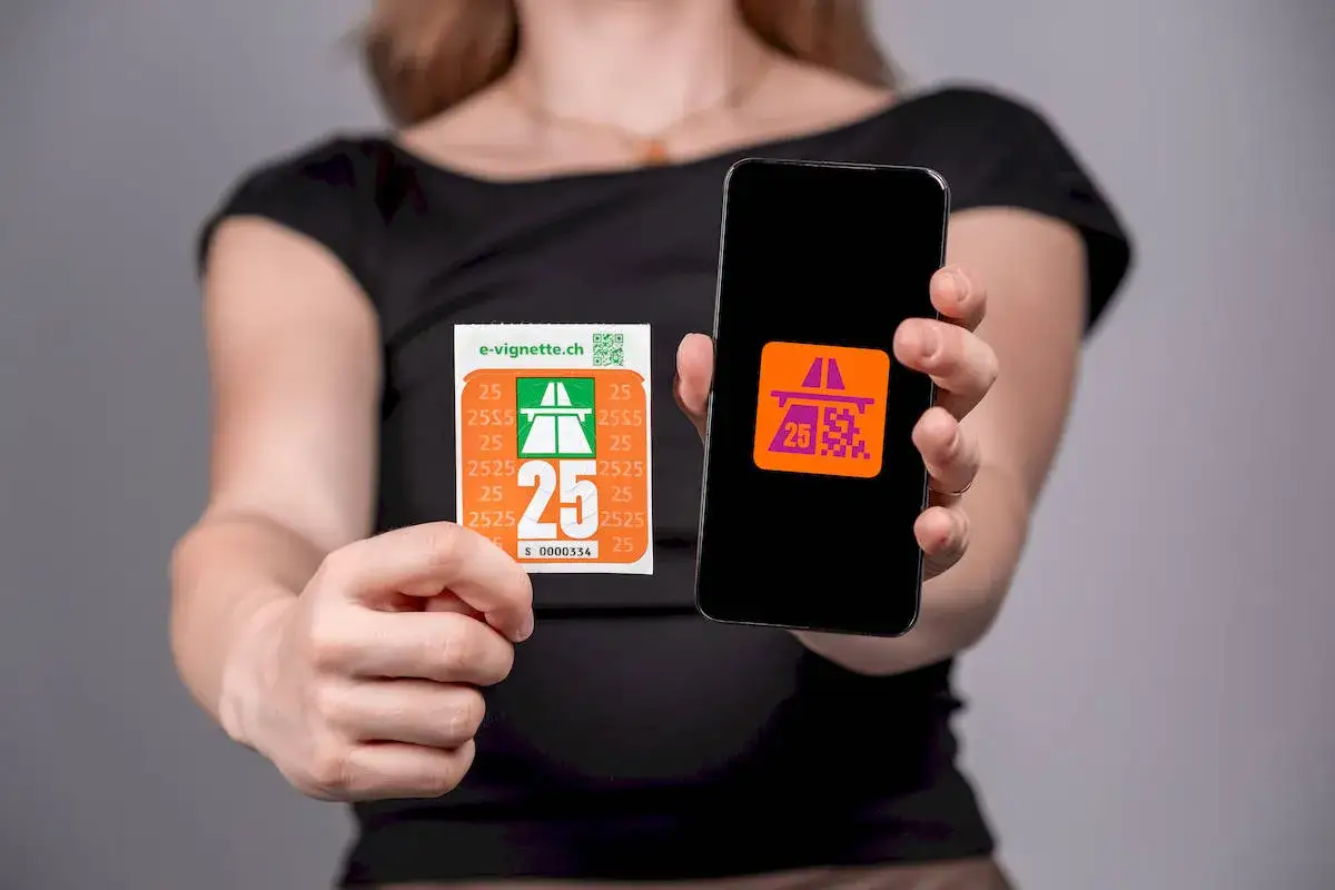 Kobieta pokazuje naklejkę i ekran telefonu z symbolem autostrady i cyfrą 25, symbolizującym winietę szwajcaria.