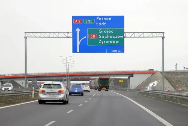 Znak drogowy informuje o minimalnej prędkości na autostradzie A2 i E30. Kierowcy zbliżają się do zjazdu na Grójec, Sochaczew i Żyrardów.