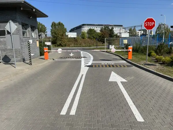 Wyraźne **znaki poziome** kierują ruch na wjeździe, gdzie szlabany i znak STOP zapowiadają kontrolę.