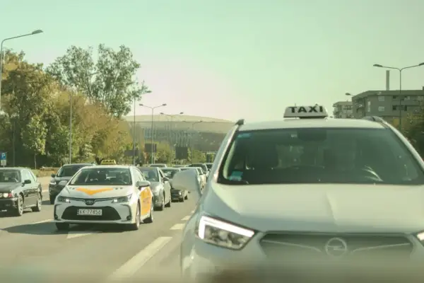 Rząd samochodów, w tym taksówek, na drodze w słoneczny dzień.