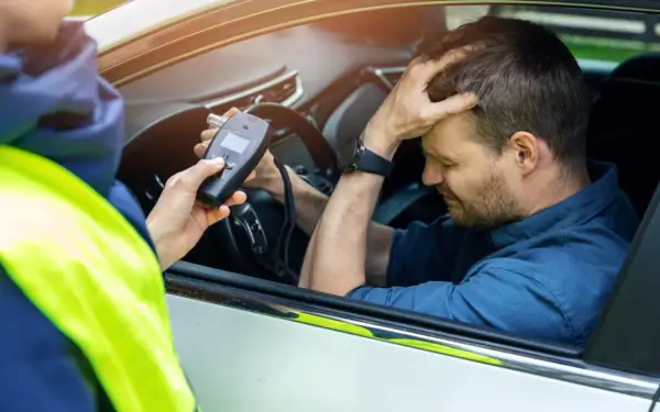 Policjant mierzy kierowcy ile promili. Mężczyzna zmartwiony trzyma się za głowę.