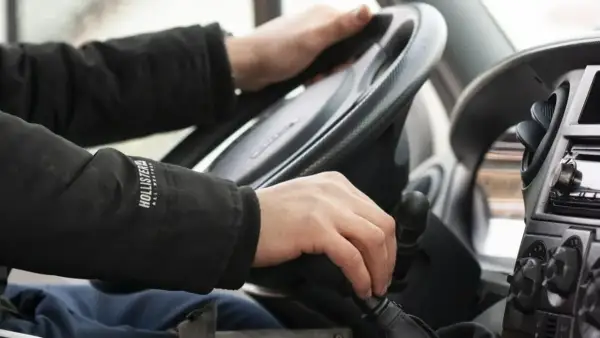 Ręce kierowcy na kierownicy i drążku zmiany biegów. Na drodze obowiązuje zakaz wyprzedzania.