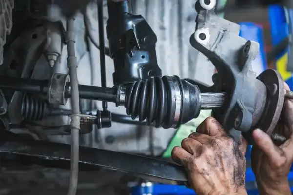 Mechanik wymienia przegub w samochodzie. Widoczny jest wałek napędowy z gumową osłoną i wielowypustem.
