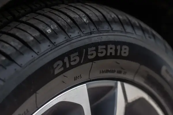 Zbliżenie na oponę z widocznym rozmiarem 215/55R18. Na boku opony można dostrzec oznaczenia dotyczące daty produkcji.